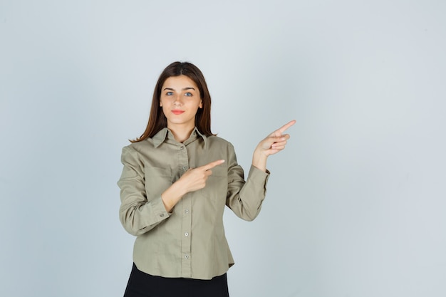 Giovane donna che punta all'angolo in alto a destra in camicia, gonna e sembra soddisfatta