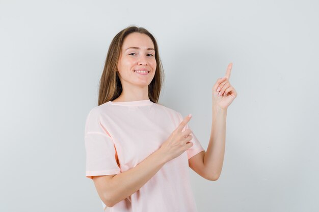Giovane donna che punta all'angolo in alto a destra in maglietta rosa e sembra gioviale
