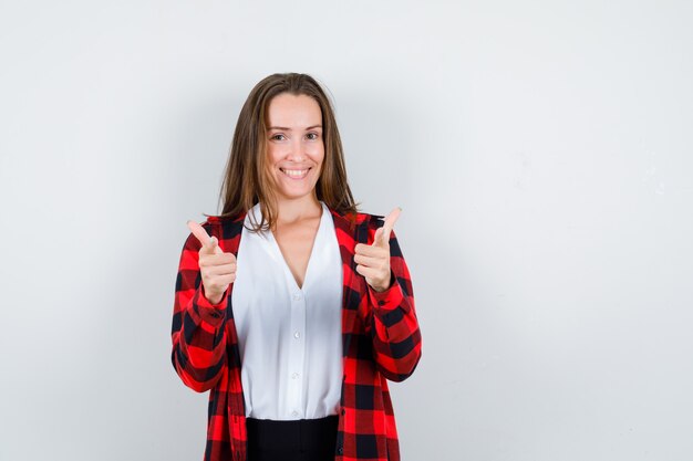 Giovane donna che punta alla telecamera in abiti casual e sembra gioviale. vista frontale.