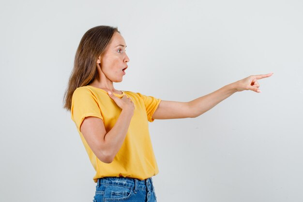 Giovane donna che punta il dito in avanti con la mano sul petto in t-shirt, pantaloncini vista frontale.