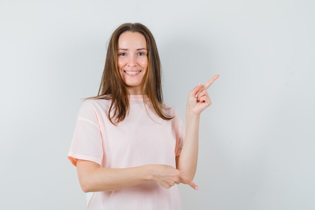 Giovane donna che punta le dita su e giù in maglietta rosa e sembra gioiosa, vista frontale.