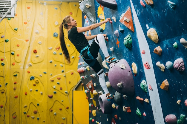 Giovane donna che scala una parete di roccia alta, indoor, artificiale