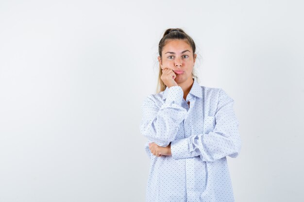 Giovane donna che si appoggia la guancia sul pugno, incurvando le labbra in camicia bianca e guardando deluso