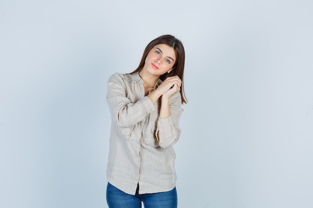 Giovane donna che si appoggia la testa sulle mani giunte in casual, jeans e dall'aspetto fiducioso. vista frontale.