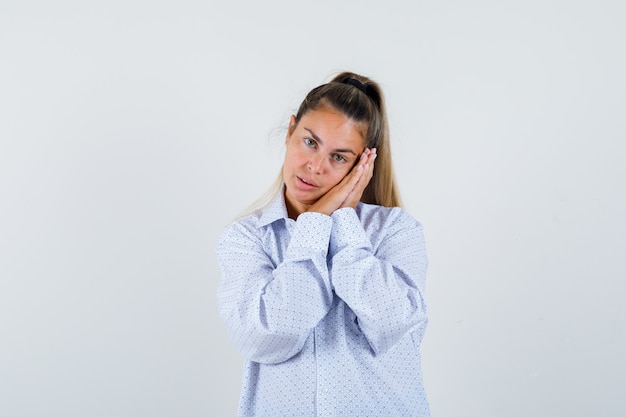 Giovane donna che si appoggia sulla guancia sui palmi come cuscino in camicia bianca e che sembra carina