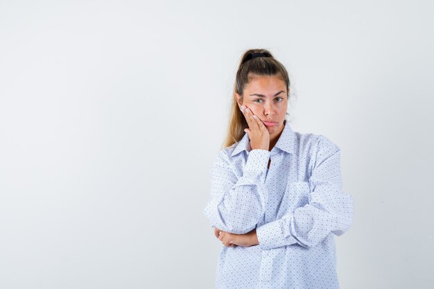 Giovane donna che si appoggia sulla guancia sul palmo in camicia bianca e sembra carino