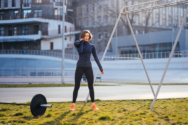 Giovane donna che si esercita con un kettlebell fuori allo stadio