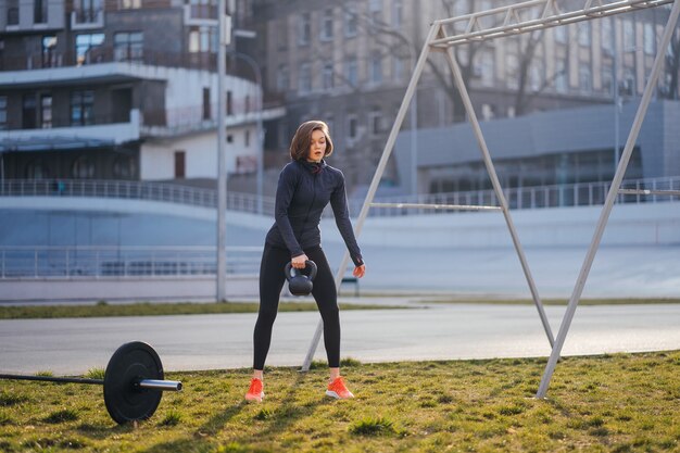 Giovane donna che si esercita con un kettlebell fuori allo stadio