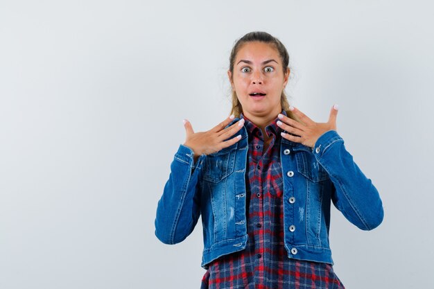 Giovane donna che si mostra nel gesto interrogativo in camicia, giacca e sembra felice, vista frontale.