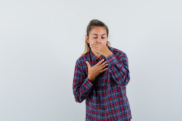 Giovane donna che si sente nauseata in camicia a quadri e non sembra stare bene. vista frontale.