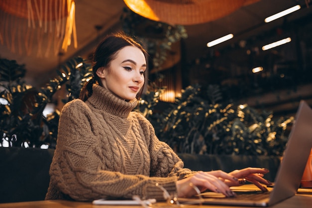 Giovane donna che si siede nella caffetteria e lavora al computer portatile