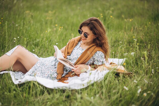 Giovane donna che si siede sull'erba in parco e libro resing