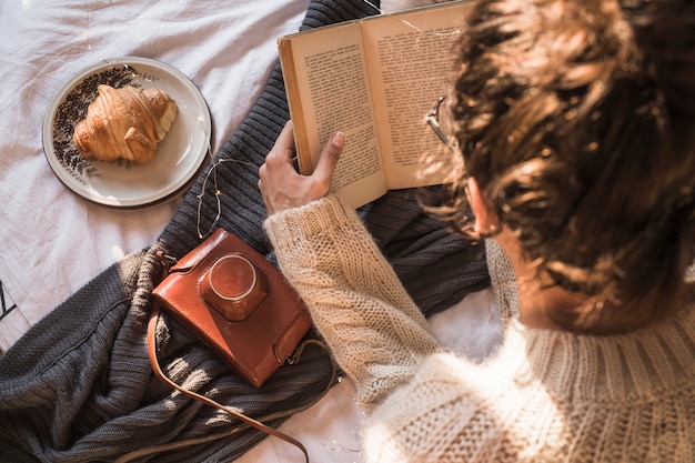 Giovane donna che si siede sulla coperta e sul libro di lettura