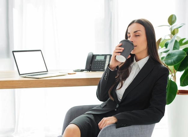 Giovane donna che si siede sulla sedia alla scrivania che gode del caffè