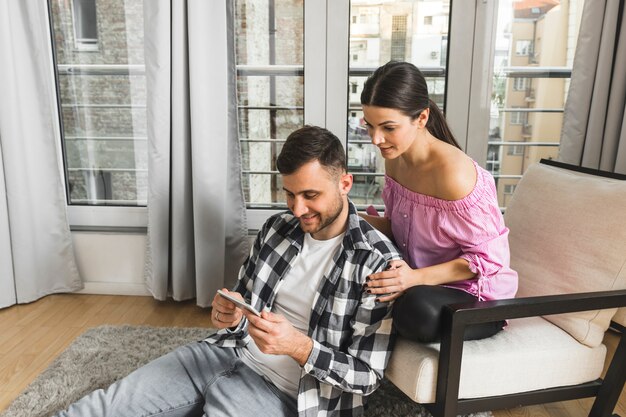 Giovane donna che si siede sulla sedia guardando il suo fidanzato utilizzando il telefono cellulare a casa