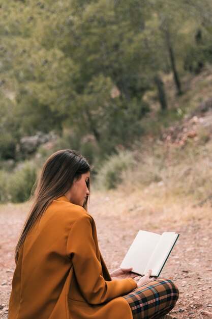 Giovane donna che si siede sulla terra leggendo il libro