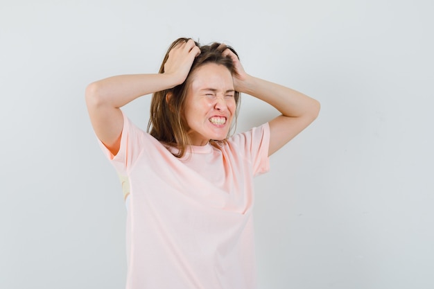 Giovane donna che si strappa i capelli in maglietta rosa e sembra frustrata. vista frontale.