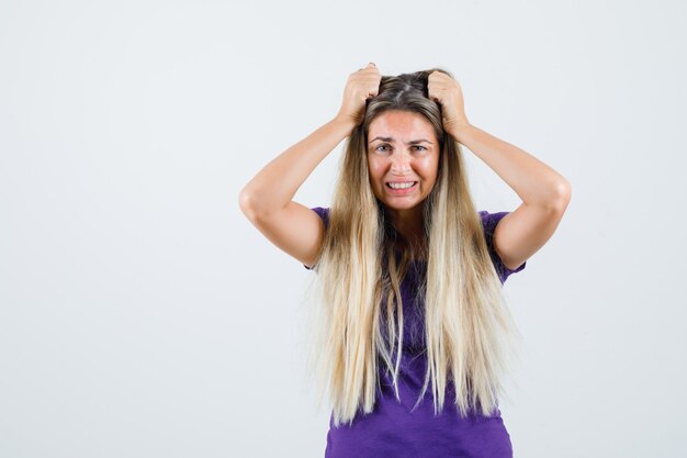 Giovane donna che si tiene per mano alla testa in maglietta viola e guardando malinconico, vista frontale.