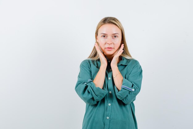 Giovane donna che si tiene per mano vicino alle guance in camicia verde e sembra delicata.