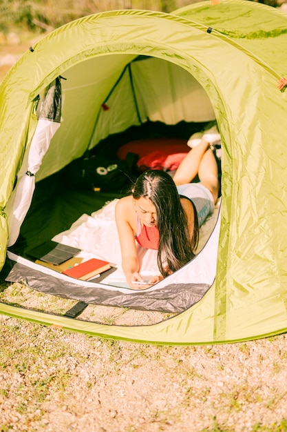 Giovane donna che si trova in tenda con lo smartphone