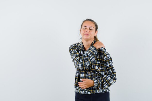 Giovane donna che soffre di dolore alla spalla in maglietta, pantaloncini e sembra stanca, vista frontale.