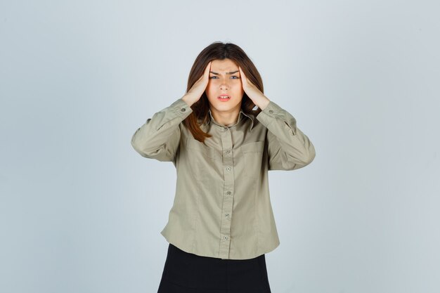 Giovane donna che soffre di forte mal di testa in camicia e sembra infastidita