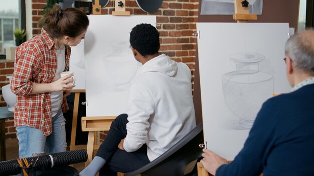 Giovane donna che spiega lezione artistica allo studente in classe d'arte. Uomo creativo che usa matita e tela con cavalletto, disegnando un capolavoro di vaso per apprendere nuove abilità in officina con l'insegnante.