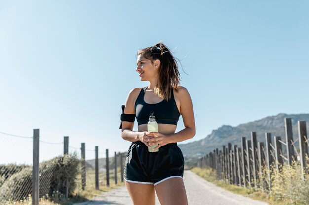 Giovane donna che sta e che tiene bottiglia di acqua