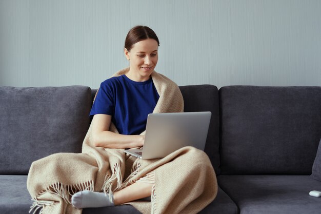 Giovane donna che stringe a sé in una coperta calda con un computer portatile