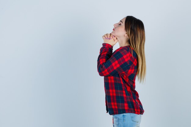 Giovane donna che stringe le mani nel gesto di preghiera in camicia a quadri e sembra speranzosa. .