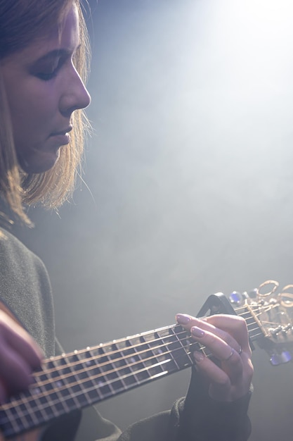 Giovane donna che suona la chitarra acustica in una stanza buia con foschia