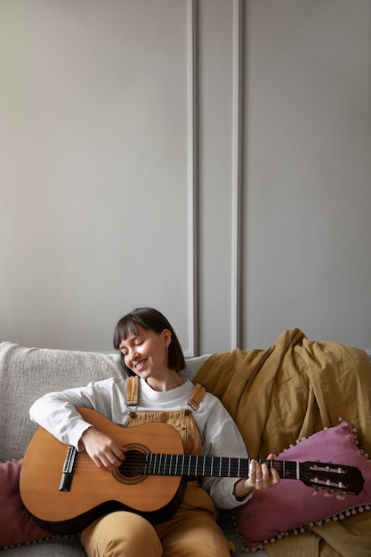 Giovane donna che suona la chitarra in casa con spazio di copia