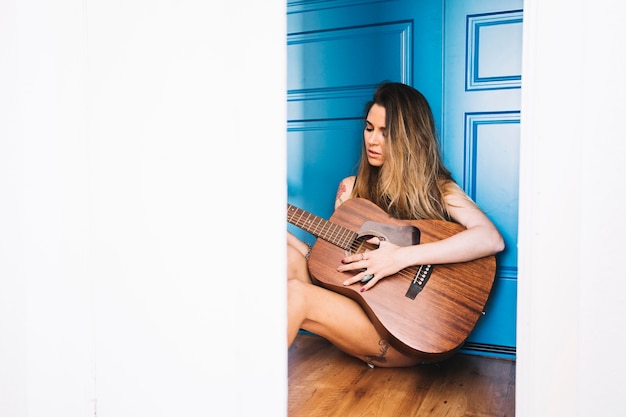 Giovane donna che suona la chitarra sul pavimento