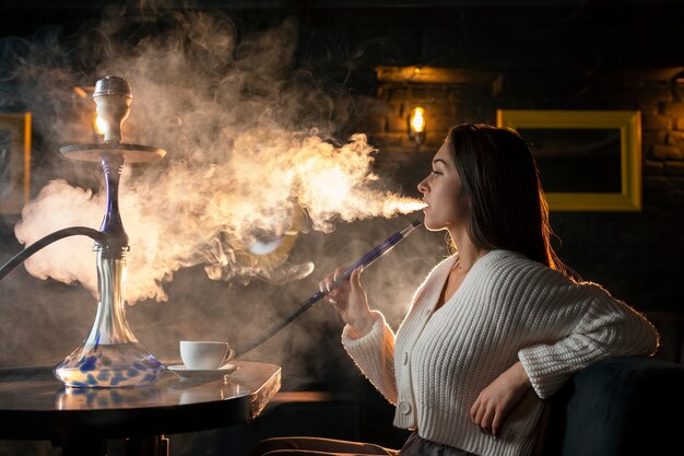 Giovane donna che svapa da un narghilè in un bar