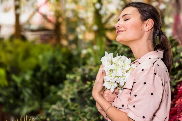 Giovane donna che tiene fiore bianco in serra