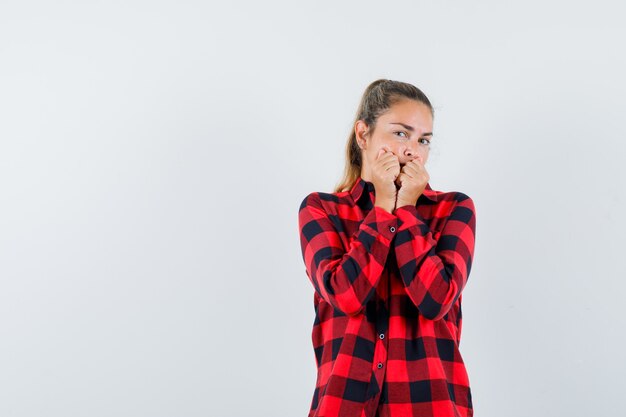 Giovane donna che tiene i pugni sulla bocca in camicia a quadri e sembra spaventata