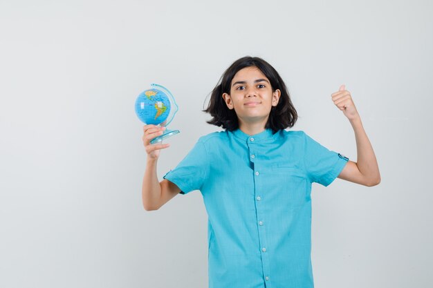 Giovane donna che tiene il mini globo mentre mostra il gesto del vincitore in camicia blu e che sembra soddisfatto.