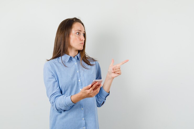 Foto gratuito giovane donna che tiene il telefono cellulare mentre punta lontano in maglietta blu e guardando concentrato.