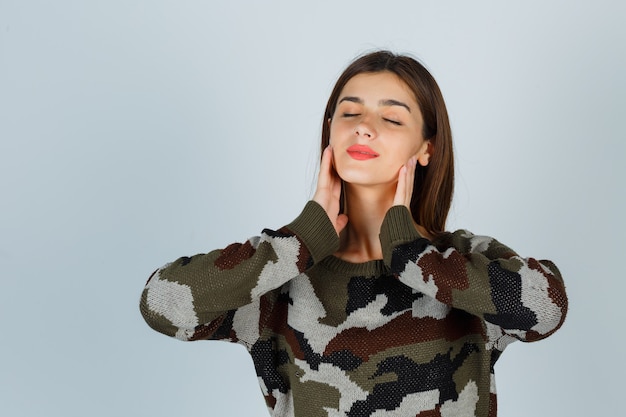 Giovane donna che tiene la mano sotto il mento in maglione, gonna e sembra pacifica