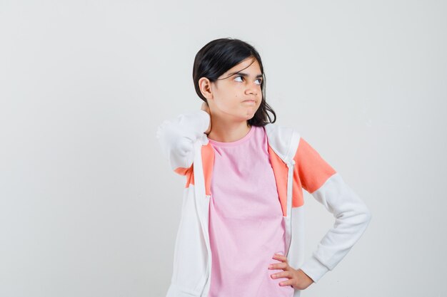 Giovane donna che tiene la mano sul collo mentre guarda da parte in giacca, camicia rosa e sembra arrabbiata.