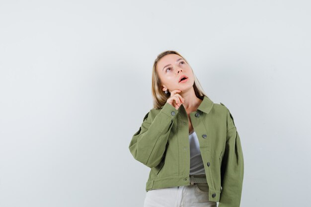 Giovane donna che tiene la mano sul mento in giacca, pantaloni e guardando pensieroso, vista frontale.