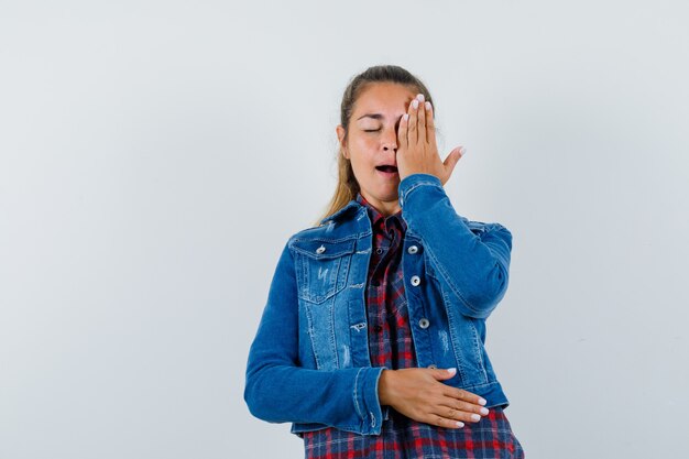 Giovane donna che tiene la mano sull'occhio in camicia, giacca e guardando speranzoso, vista frontale.