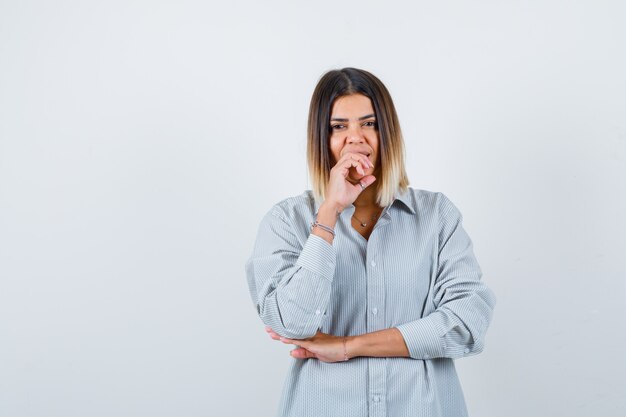 Giovane donna che tiene la mano sulla bocca in camicia oversize e sembra soddisfatta. vista frontale.