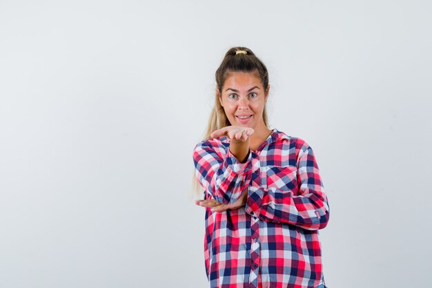 Giovane donna che tiene la mano tesa in camicia a quadri e sembra allegra, vista frontale.