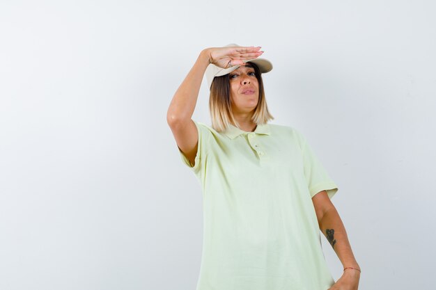 Giovane donna che tiene la mano vicino al cappuccio per vedere chiaramente in t-shirt, cappuccio e guardare fiducioso. vista frontale.