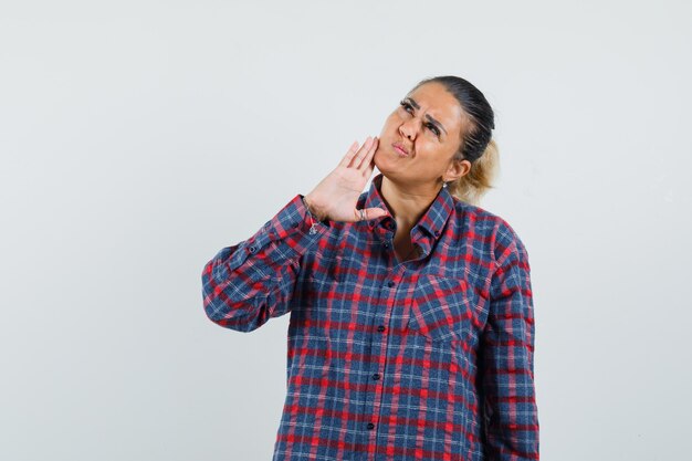 Giovane donna che tiene la mano vicino al mento, pensando a qualcosa in camicia a quadri e guardando pensieroso. vista frontale.