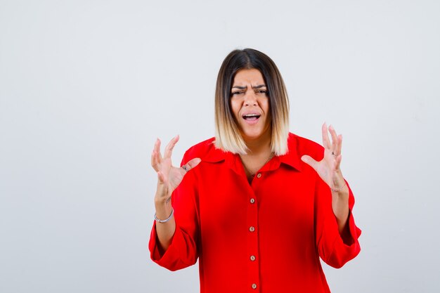 Giovane donna che tiene le mani in modo aggressivo in una camicia oversize rossa e sembra infastidita. vista frontale.