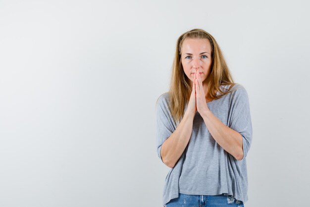 Giovane donna che tiene le mani in preghiera su sfondo bianco