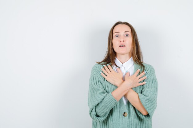 Giovane donna che tiene le mani incrociate sul petto in camicia, cardigan e sembra perplessa. vista frontale.