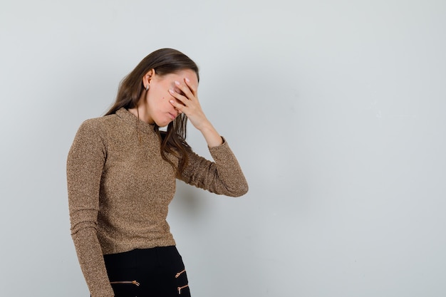 Giovane donna che tiene le mani sugli occhi in camicetta dorata e guardando annoiato, vista frontale. spazio per il testo